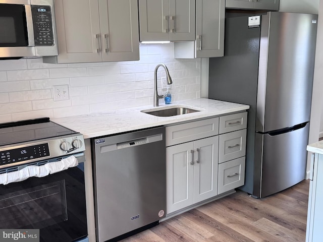 kitchen with light stone counters, a sink, light wood-style floors, stainless steel appliances, and gray cabinetry