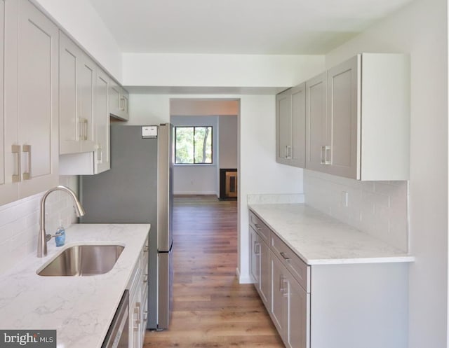 kitchen featuring light stone countertops, a sink, light wood finished floors, backsplash, and stainless steel appliances