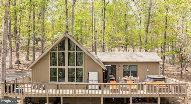 rear view of property with a forest view, a deck, and a jacuzzi