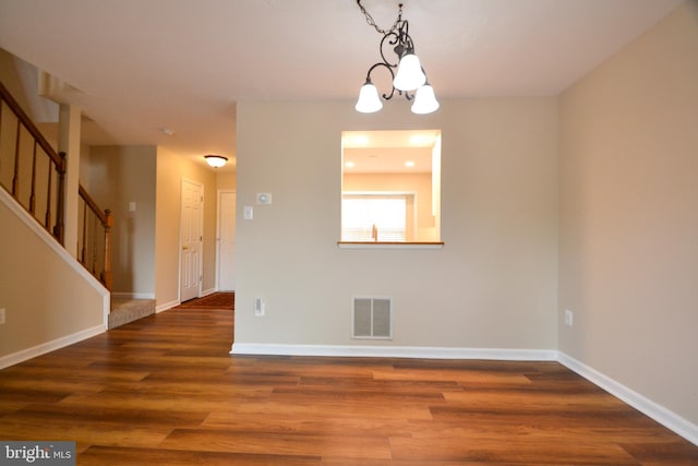 spare room with stairs, visible vents, an inviting chandelier, and wood finished floors