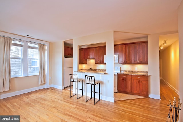 kitchen featuring light wood-style floors, a sink, a breakfast bar, and white appliances