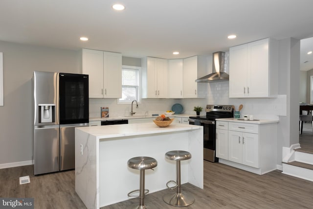 kitchen with appliances with stainless steel finishes, a center island, white cabinetry, a sink, and wall chimney exhaust hood