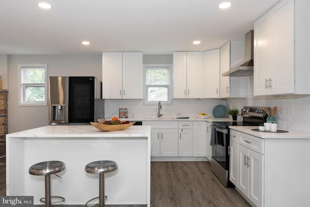 kitchen featuring wall chimney range hood, a sink, appliances with stainless steel finishes, and a healthy amount of sunlight