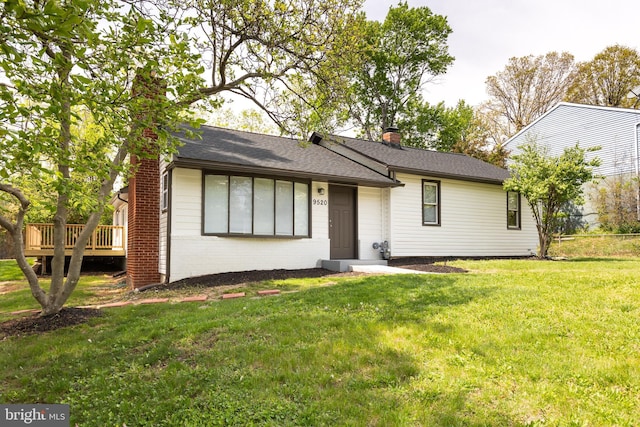 single story home featuring roof with shingles, a front lawn, brick siding, a wooden deck, and a chimney