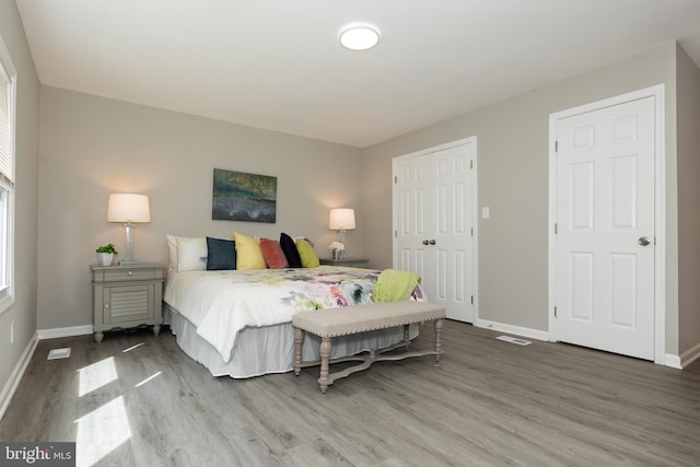 bedroom featuring baseboards, wood finished floors, visible vents, and a closet