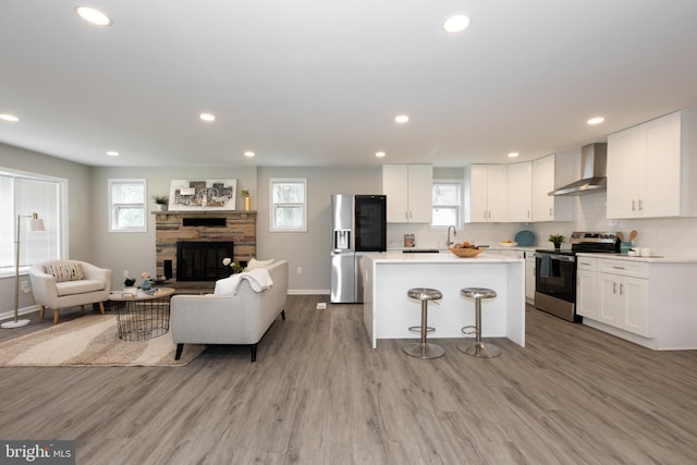kitchen with wall chimney range hood, white cabinets, appliances with stainless steel finishes, a center island, and open floor plan