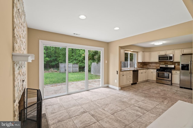 kitchen featuring stainless steel appliances, cream cabinets, baseboards, decorative backsplash, and a sink