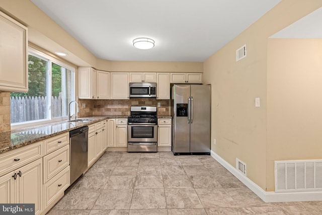 kitchen with stainless steel appliances, a sink, backsplash, and dark stone counters