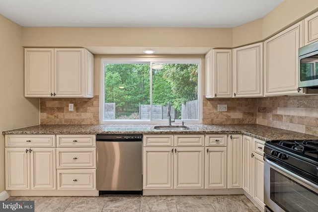 kitchen with stainless steel appliances, a sink, and dark stone counters