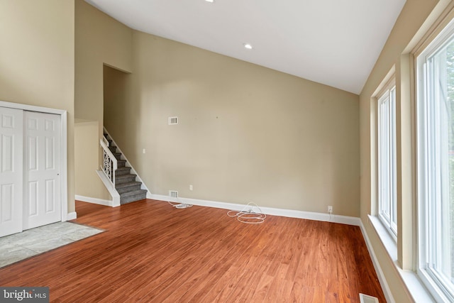 unfurnished living room featuring lofted ceiling, light wood-style floors, stairs, and baseboards