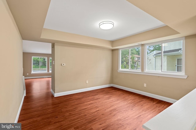 empty room with wood finished floors, a raised ceiling, and baseboards