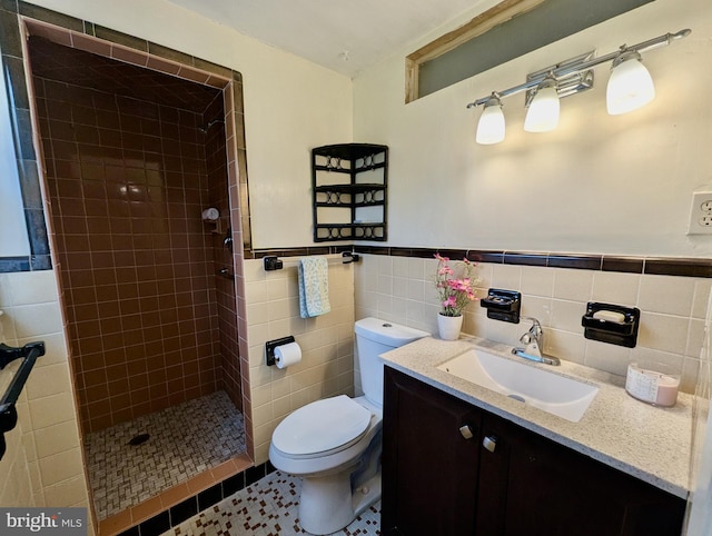 full bath featuring tile walls, vanity, toilet, a tile shower, and wainscoting