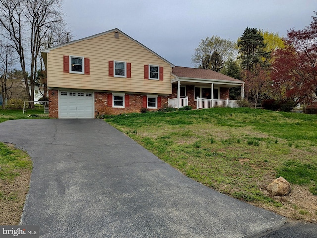 split level home featuring a porch, a front yard, brick siding, aphalt driveway, and an attached garage