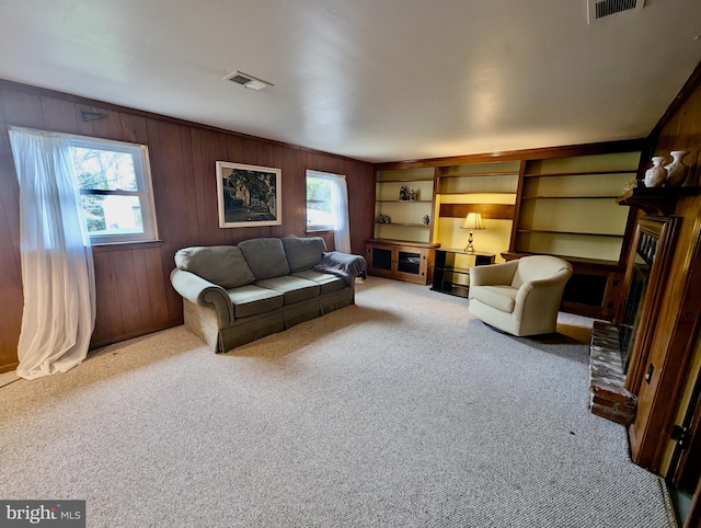 carpeted living area with visible vents, wooden walls, and a brick fireplace