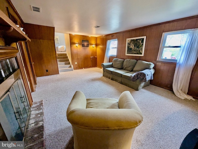 carpeted living room with wooden walls, visible vents, and stairway