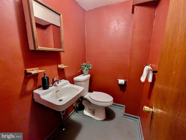 bathroom with toilet, a sink, and concrete flooring