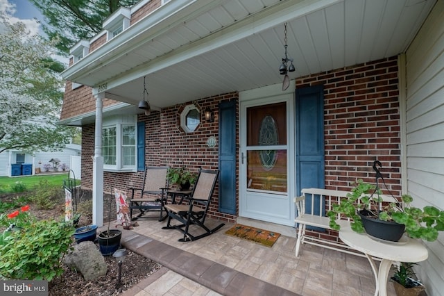 entrance to property featuring a porch and brick siding