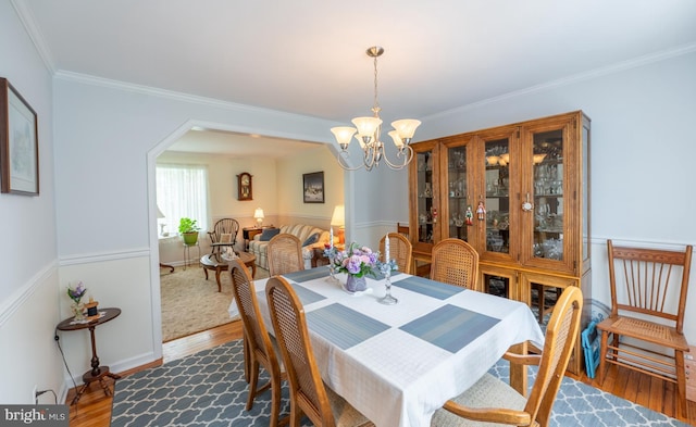 dining space featuring an inviting chandelier, ornamental molding, arched walkways, and wood finished floors