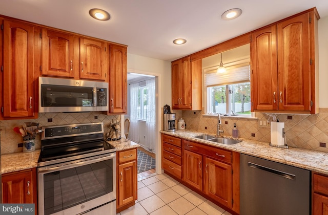kitchen featuring decorative backsplash, appliances with stainless steel finishes, light stone countertops, a sink, and light tile patterned floors