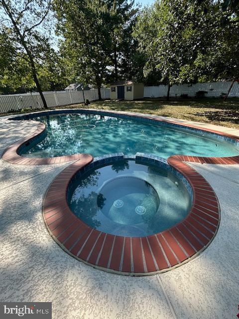 view of swimming pool featuring a fenced backyard, a storage unit, an outdoor structure, and a pool with connected hot tub