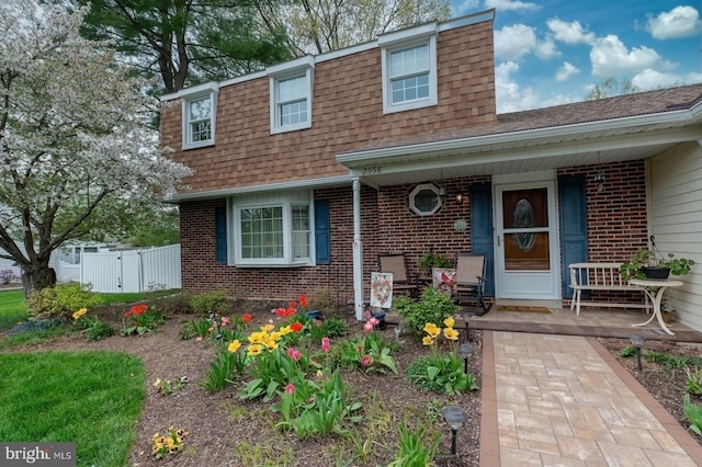 view of front of home with fence, brick siding, a shingled roof, a gate, and a porch