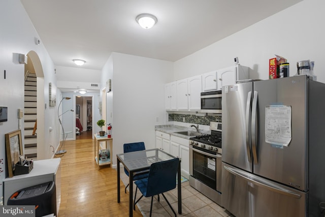 kitchen with stainless steel appliances, white cabinetry, tasteful backsplash, a sink, and arched walkways