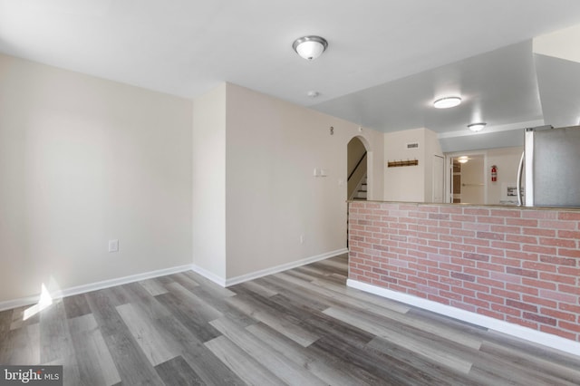 unfurnished room with wood finished floors, arched walkways, baseboards, and stairway