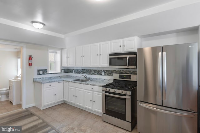 kitchen with stainless steel appliances, a sink, white cabinets, light stone counters, and baseboards