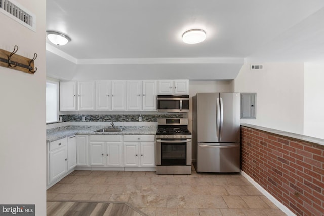 kitchen with stainless steel appliances, a sink, white cabinetry, electric panel, and brick wall