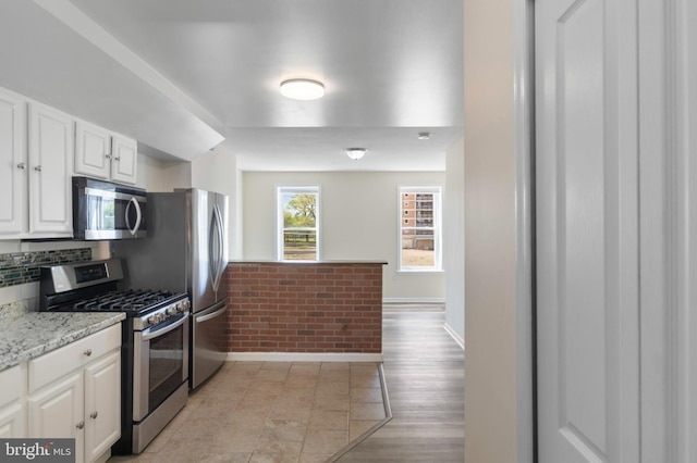 kitchen with appliances with stainless steel finishes, white cabinetry, baseboards, and tasteful backsplash