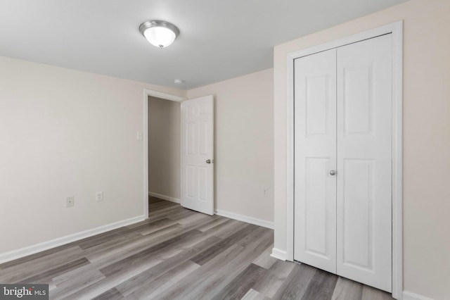 unfurnished bedroom featuring wood finished floors, baseboards, and a closet