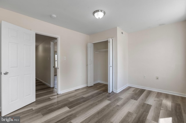 unfurnished bedroom with wood finished floors, baseboards, and a closet