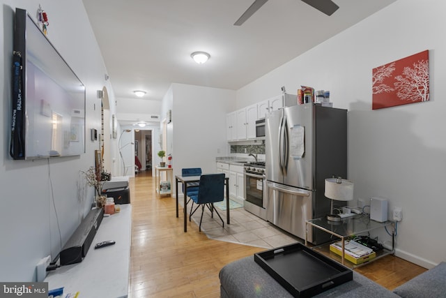 kitchen with appliances with stainless steel finishes, white cabinets, light wood finished floors, and ceiling fan