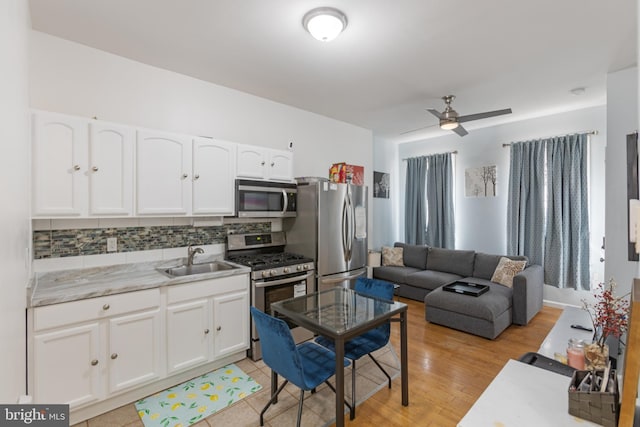 kitchen featuring appliances with stainless steel finishes, a sink, decorative backsplash, a ceiling fan, and white cabinets
