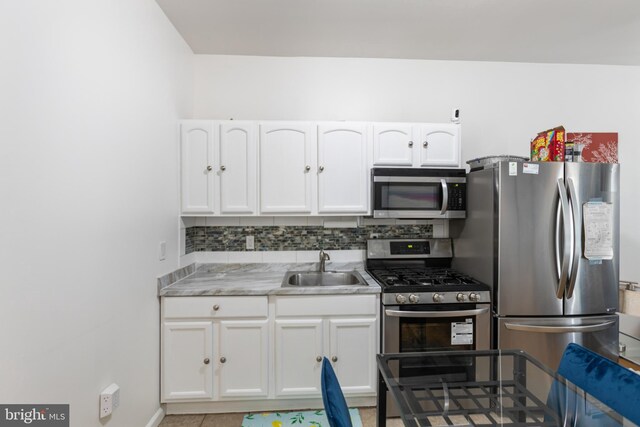kitchen featuring stainless steel appliances, a sink, white cabinetry, decorative backsplash, and light countertops