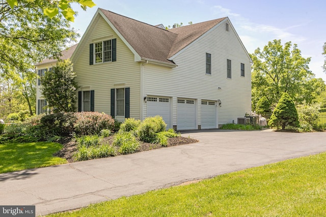 view of side of property featuring a garage, asphalt driveway, a shingled roof, and central air condition unit