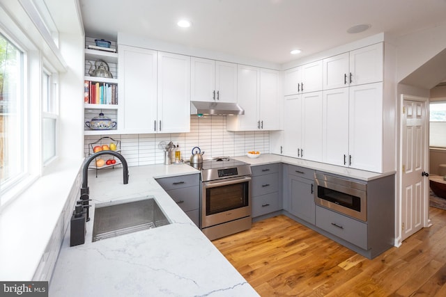 kitchen with light stone countertops, appliances with stainless steel finishes, a sink, gray cabinets, and under cabinet range hood