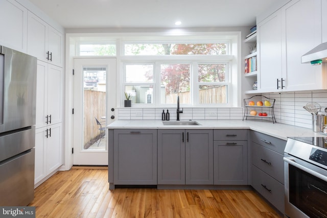 kitchen with gray cabinets, appliances with stainless steel finishes, tasteful backsplash, open shelves, and a sink