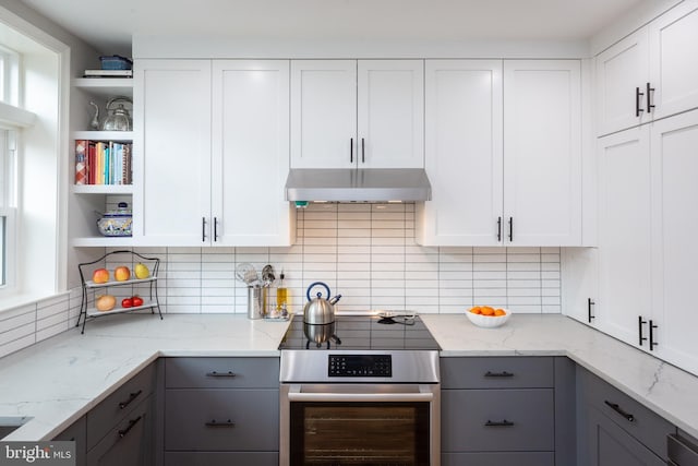 kitchen featuring under cabinet range hood, open shelves, gray cabinets, and wall oven