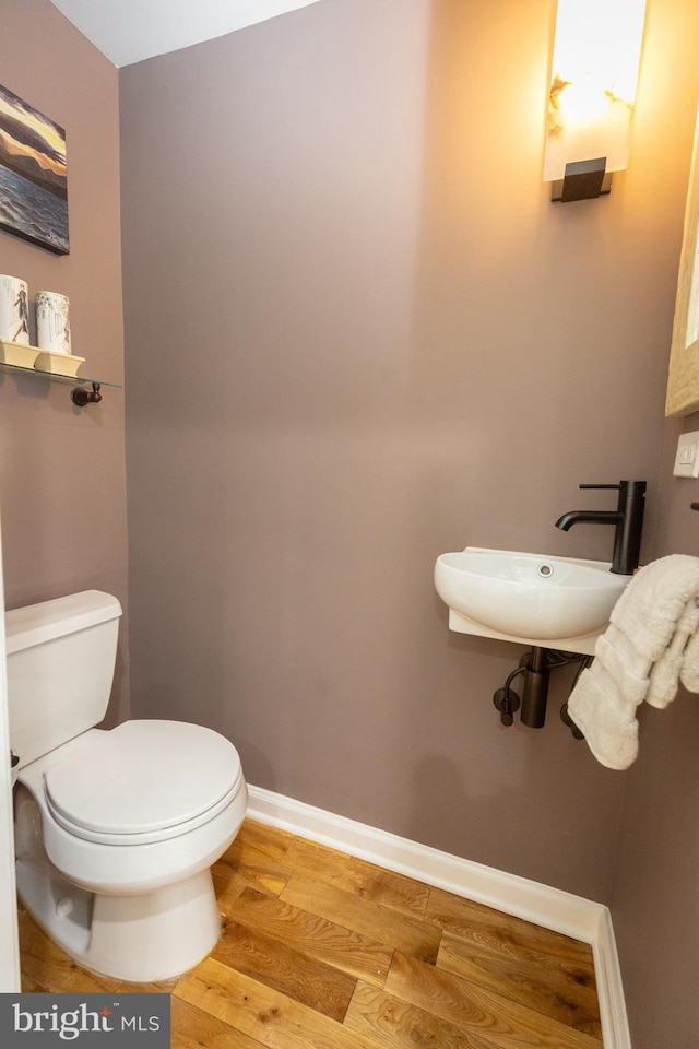 half bathroom featuring a sink, baseboards, toilet, and wood finished floors