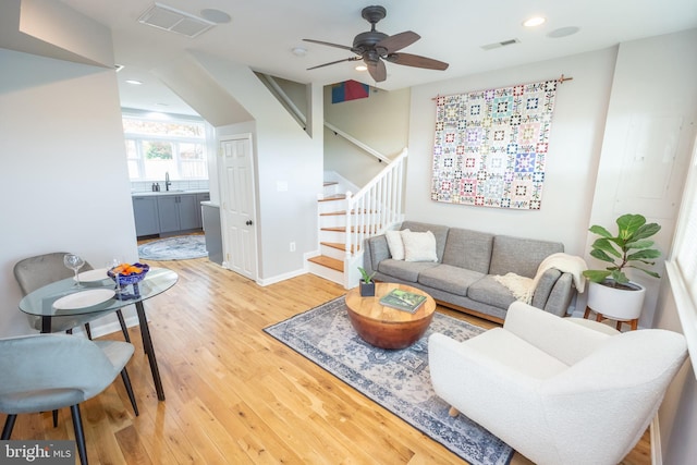 living room with stairs, ceiling fan, visible vents, and light wood-style floors