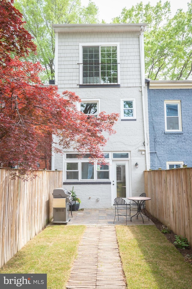 rear view of house with brick siding, a patio, a yard, and a fenced backyard