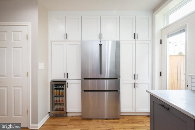 kitchen featuring wine cooler, freestanding refrigerator, light wood-type flooring, and white cabinetry