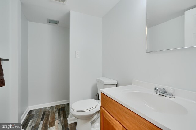 half bathroom featuring vanity, toilet, baseboards, wood finished floors, and visible vents