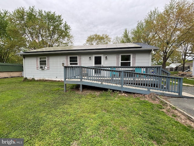 rear view of house with roof mounted solar panels, cooling unit, a wooden deck, and a yard