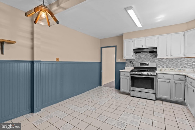 kitchen with stainless steel gas range, wainscoting, light countertops, decorative backsplash, and under cabinet range hood