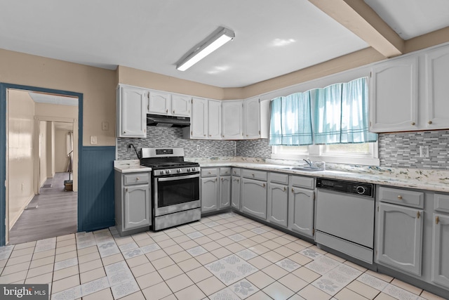 kitchen featuring stainless steel gas range, dishwasher, light countertops, under cabinet range hood, and gray cabinetry