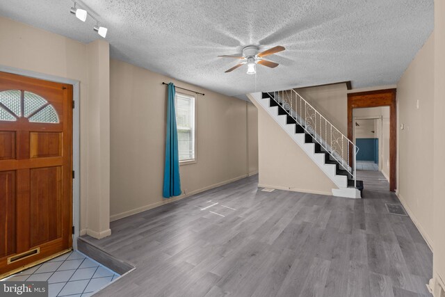foyer entrance with ceiling fan, a textured ceiling, baseboards, wood finished floors, and stairway