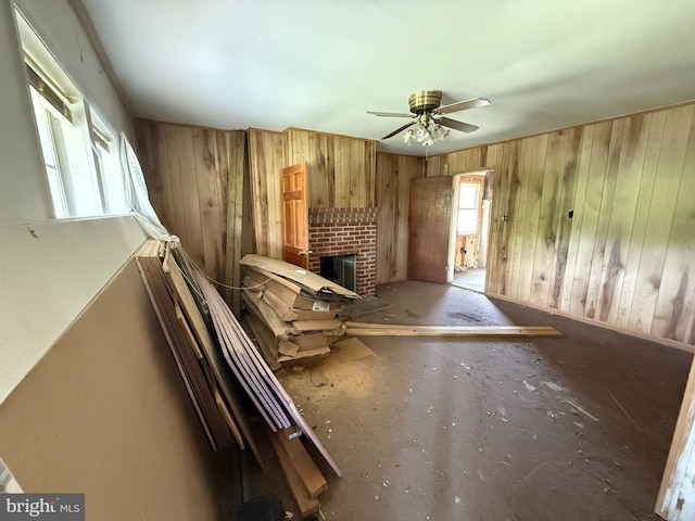 unfurnished living room featuring a brick fireplace, a ceiling fan, wood walls, and baseboards