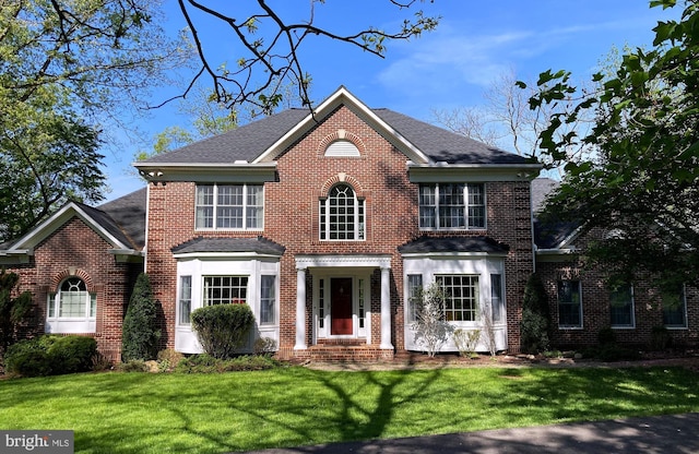 view of front of property featuring brick siding, a shingled roof, and a front lawn